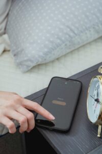 From above of hand of crop anonymous female turning off alarm on mobile phone in bedroom in morning time